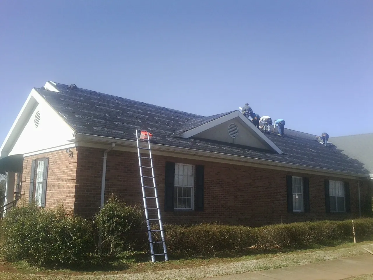 Crew tearing shingles off a brick ranch roof with a ladder set — Emergency Roof Repair work by our crew in Parachute
