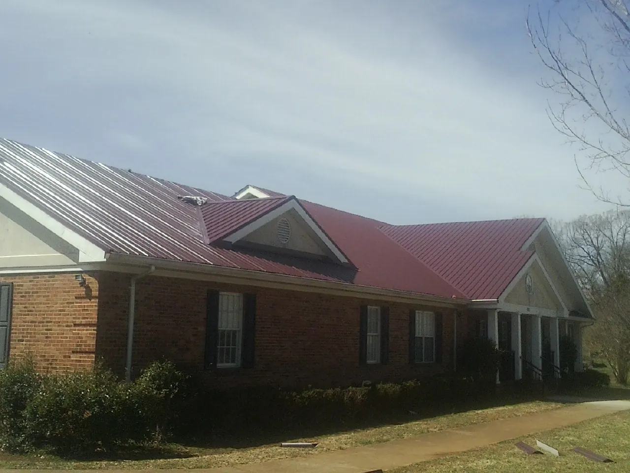 Red metal roof with gabled entries on a long brick building, from a Hail Damage Roof Repair job in Parachute