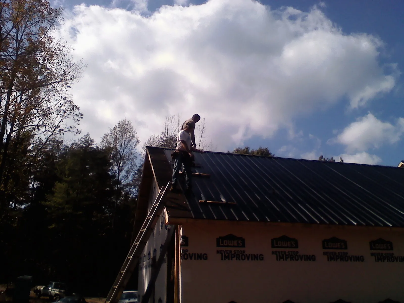 Roofer fastening dark metal panels high against a cloudy sky, from a Roof Inspection job in Parachute